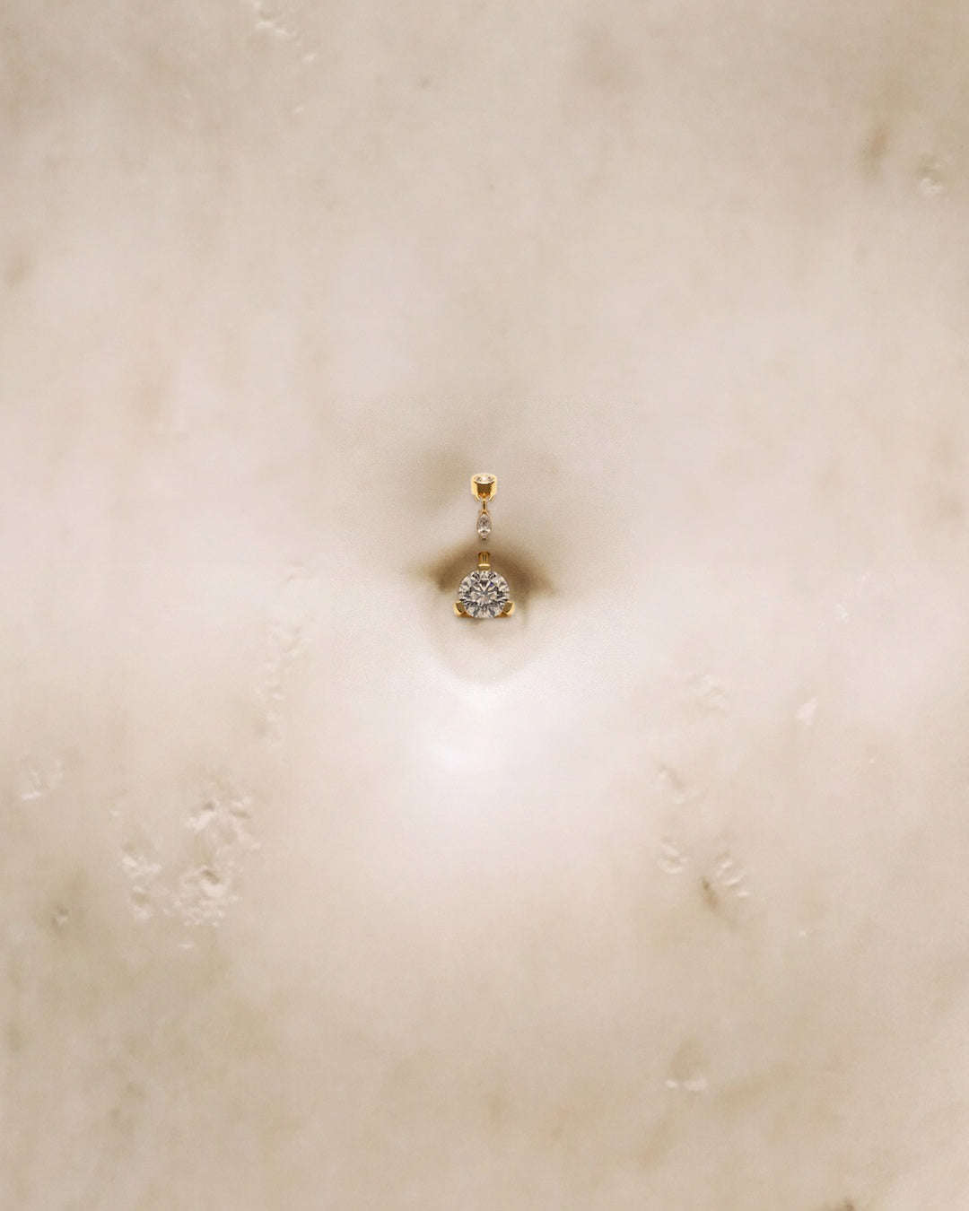 A gold belly ring with a round diamond on a white marble sculpture