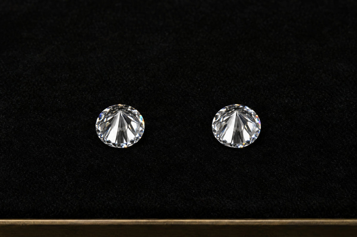 Two identical round diamonds resting table-down on a black velvet grading tray
