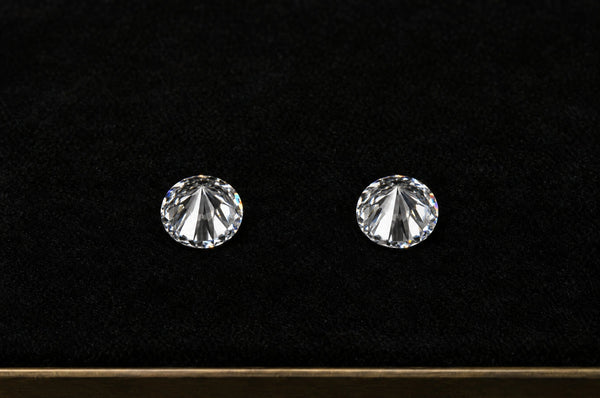 Two identical round diamonds resting table-down on a black velvet grading tray