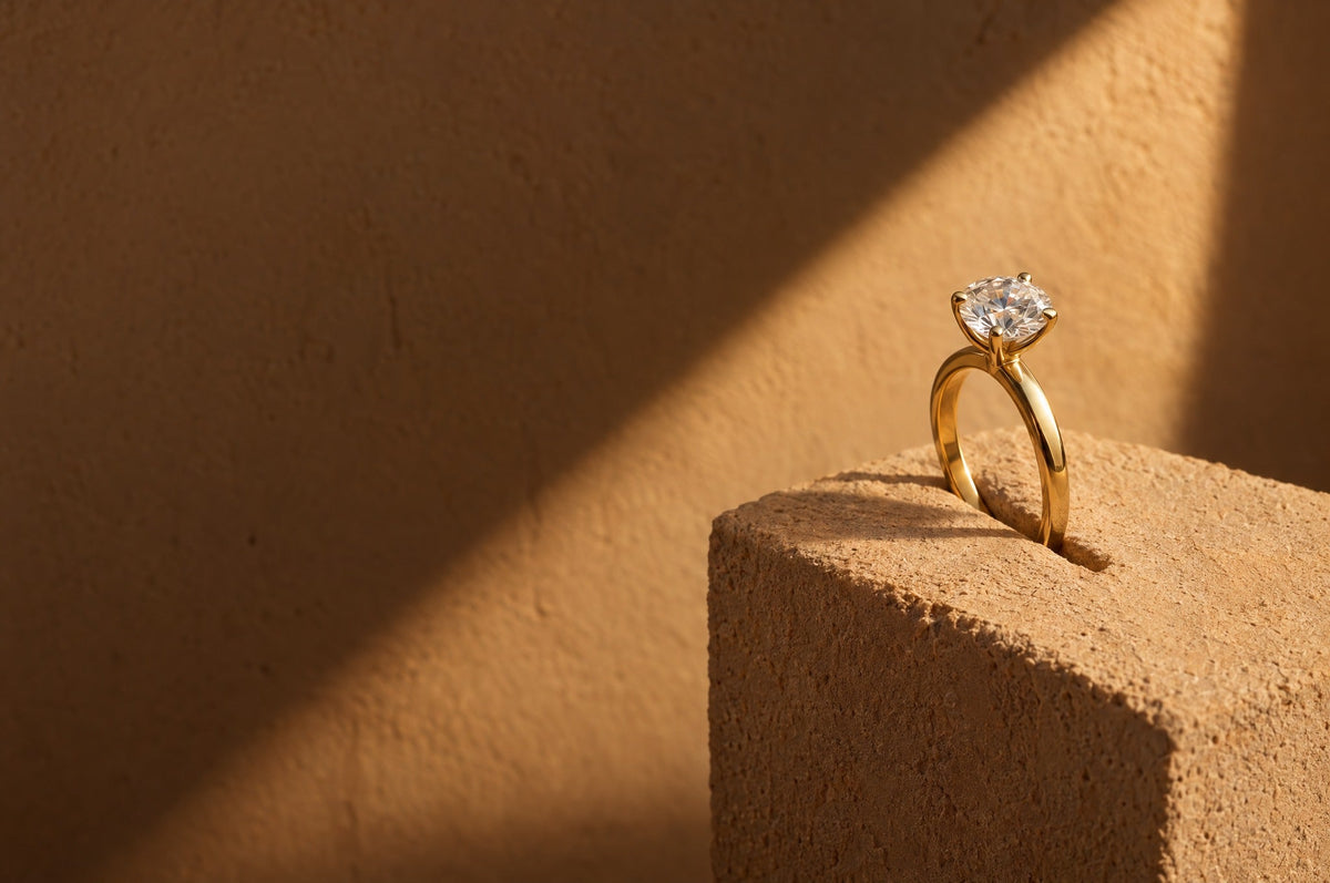 An 18K yellow gold round diamond solitaire held upright in a slit in a sand-coloured Najdi plaster block, in late-afternoon sunlight